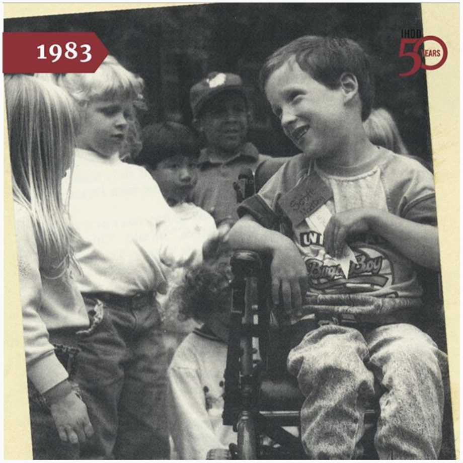 Image of children surrounding a child in a wheelchair having conversations.