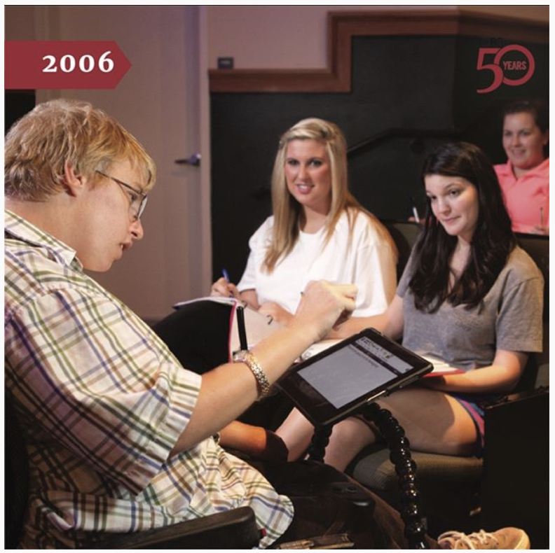 Image of a professor in a wheelchair teaching students in a classroom.